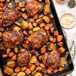 A sheet pan of chopped roasted veggies and chicken thighs fresh from the oven.