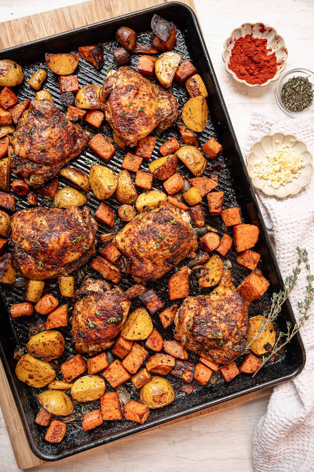 A sheet pan of chopped roasted veggies and chicken thighs fresh from the oven.
