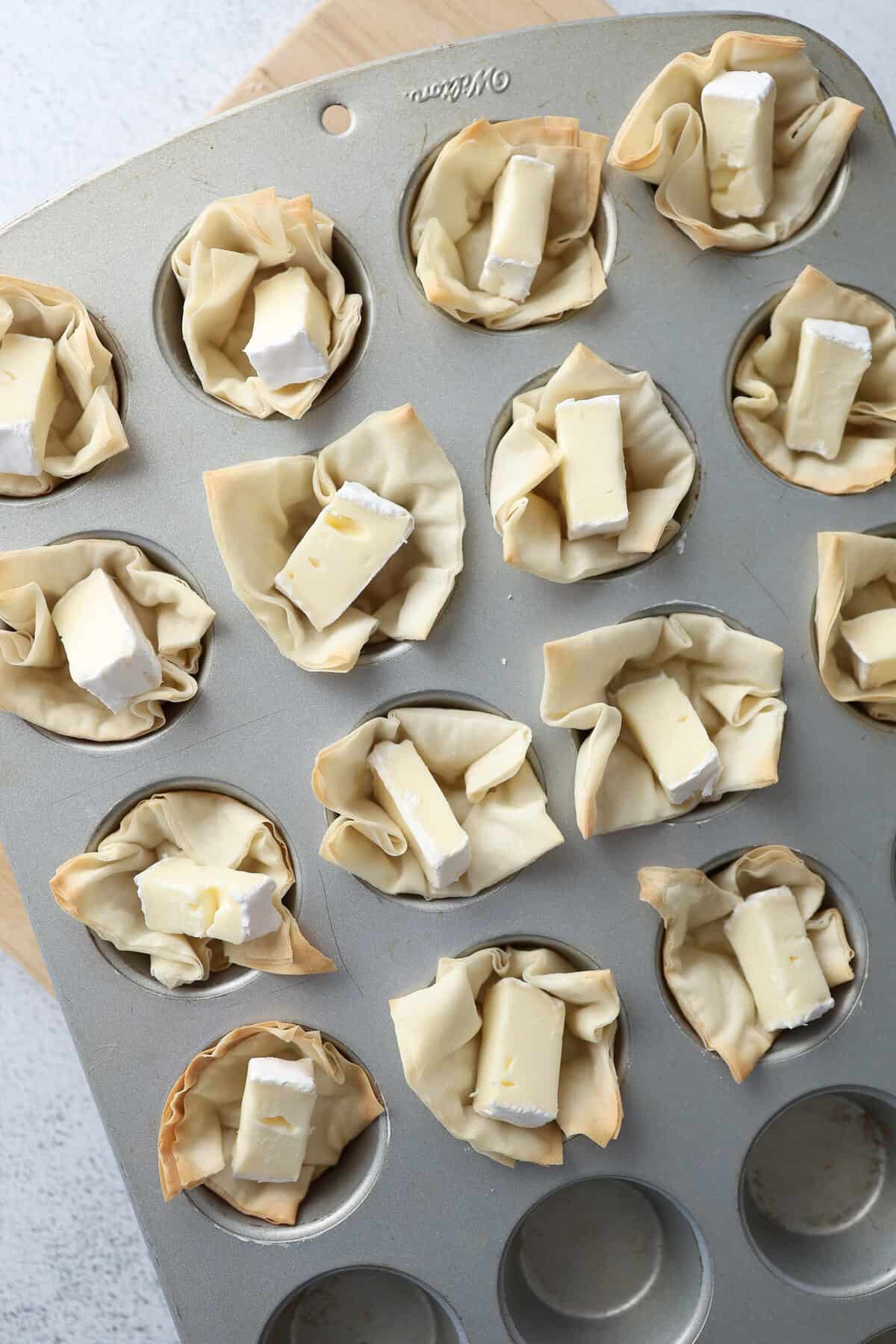 Small cut chunks of brie cheese in toasted phyllo dough cups in a mini muffin tin.