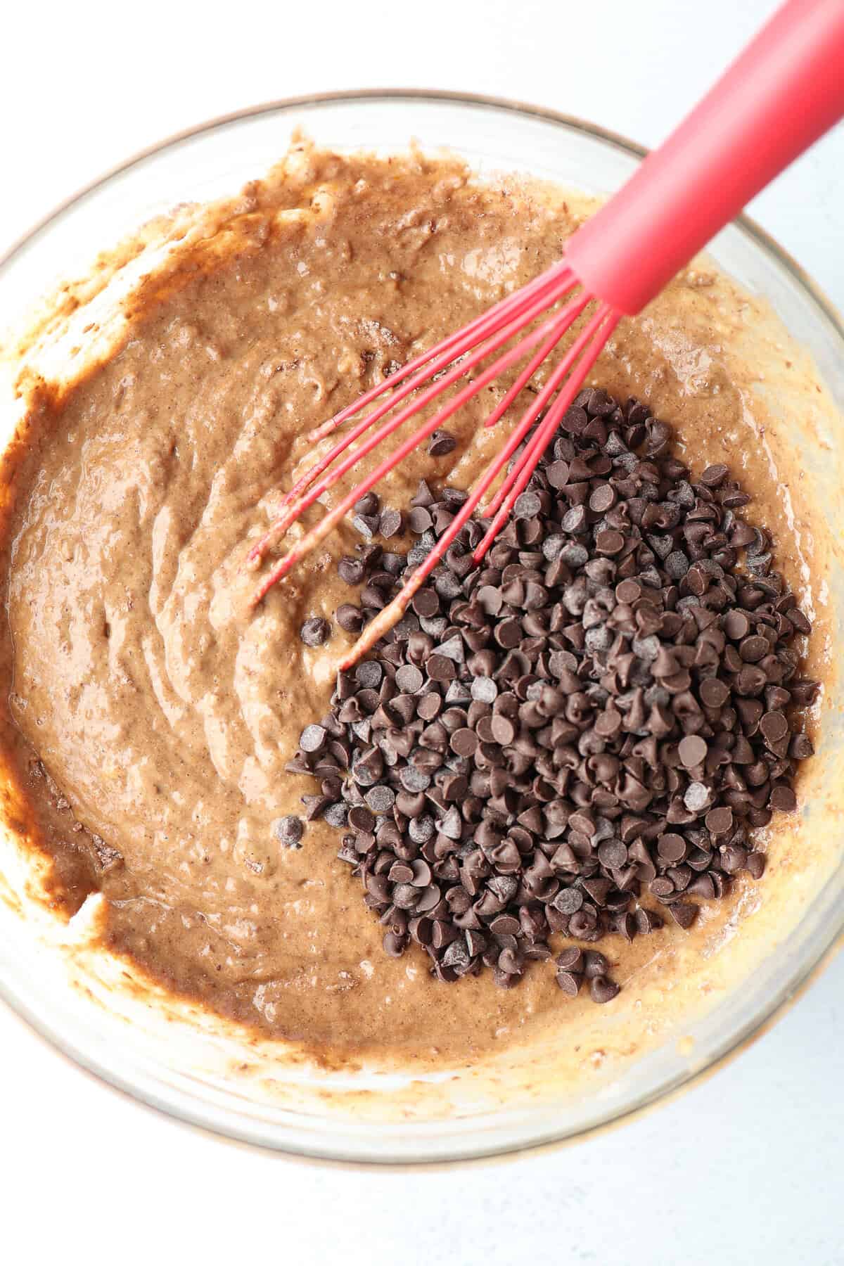Mini chocolate chips being folded into chocolate banana muffin batter with a whisk.