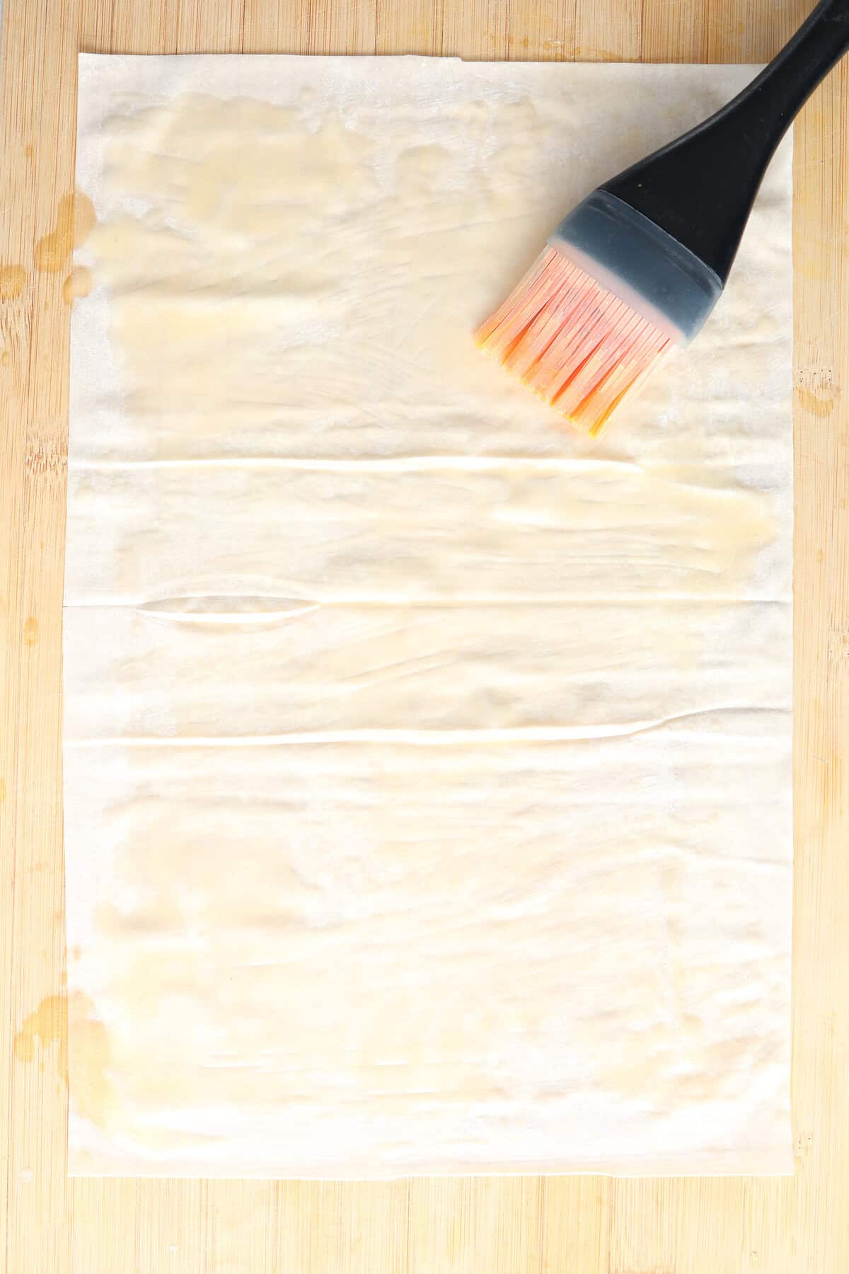 A sheet of phyllo dough being brushed with butter.