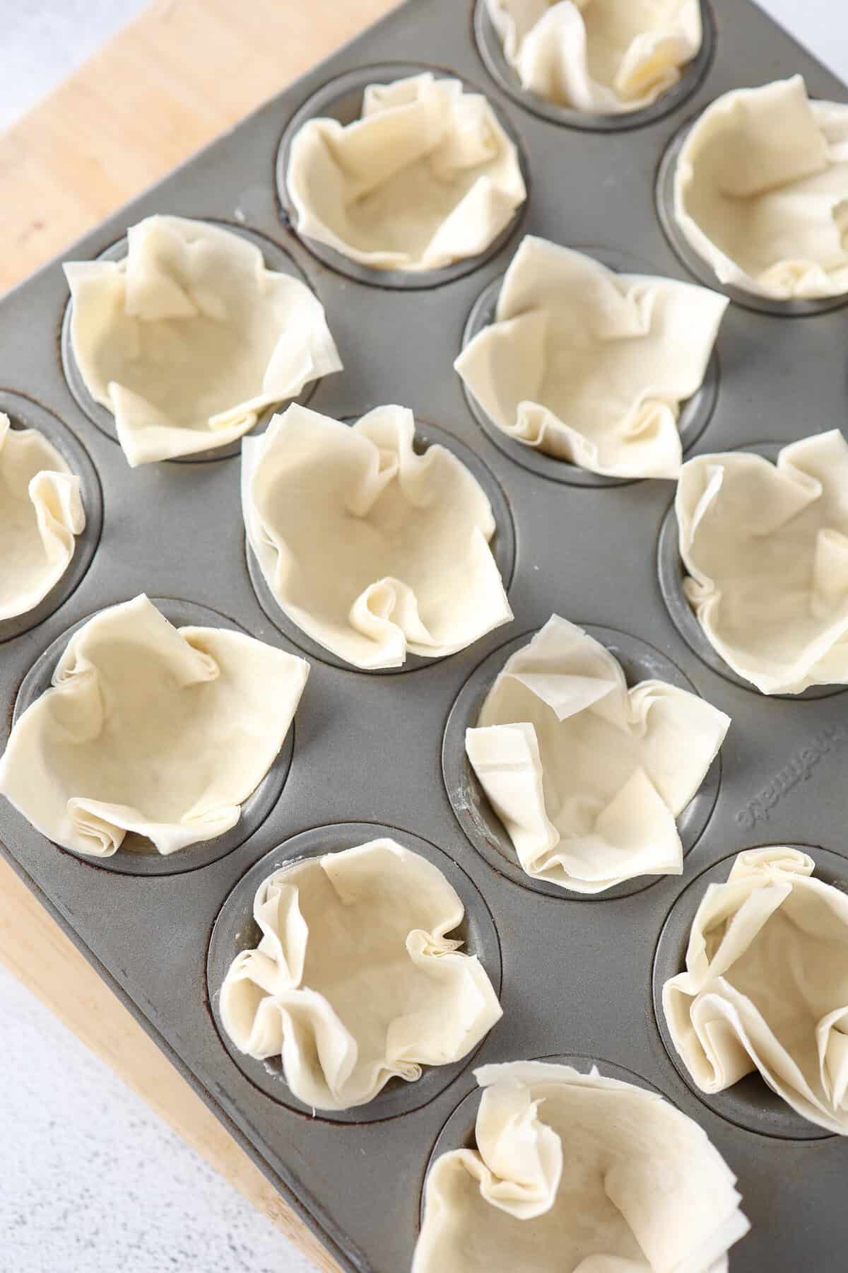 A mini muffin tin with small phyllo dough squares pushed in to make cups.
