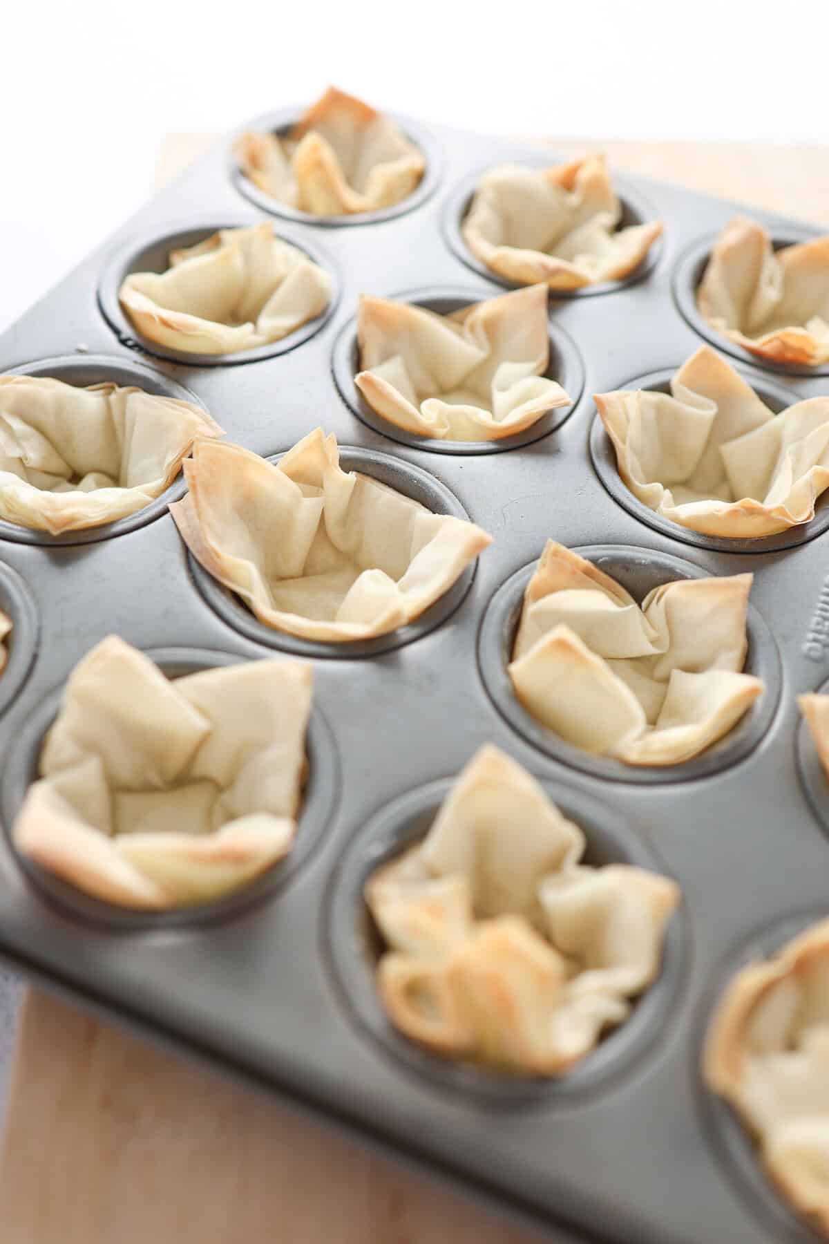 Mini phyllo cups in a mini muffin tin with toasted edges.