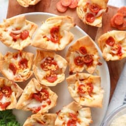 A cutting board and platter full of mini pepperoni pizza phyllo cups.