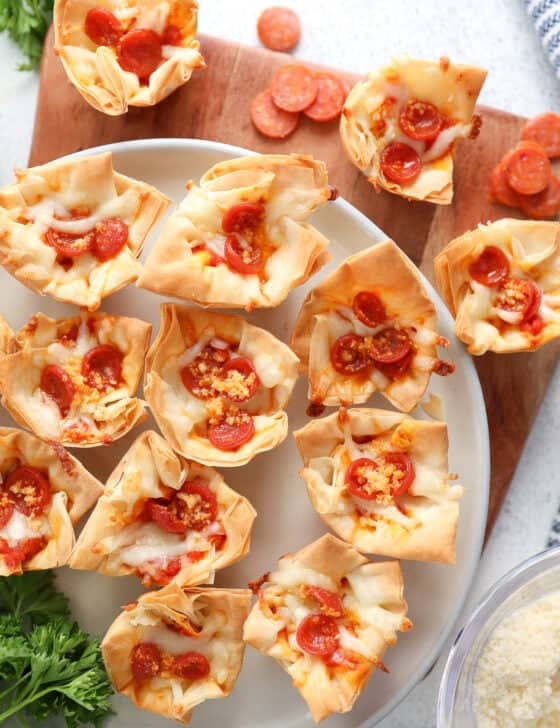 A cutting board and platter full of mini pepperoni pizza phyllo cups.