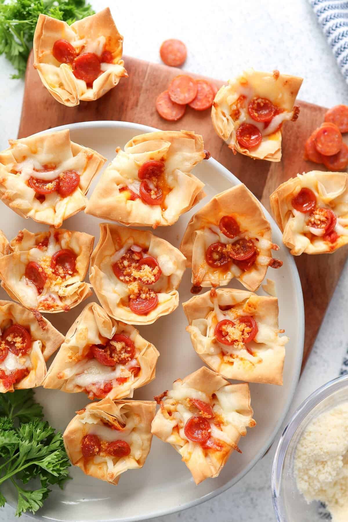 A cutting board and platter full of mini pepperoni pizza phyllo cups.