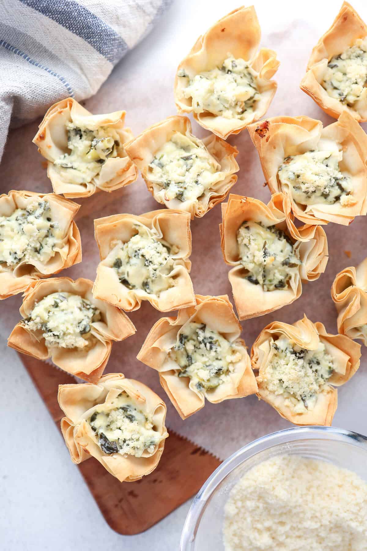 Mini spinach and artichoke phyllo cups lined up on parchment paper.