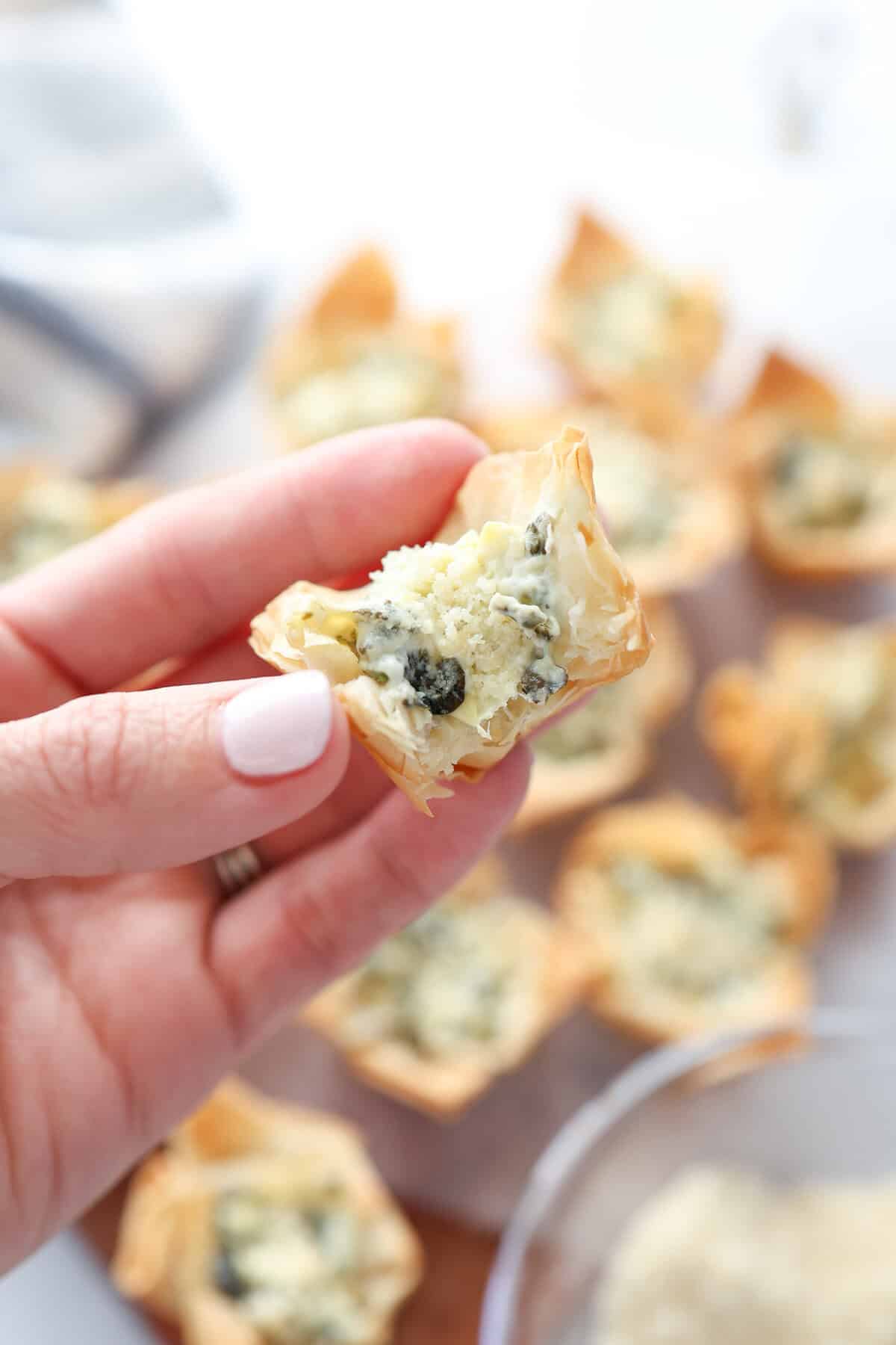A hand holding a mini spinach and artichoke phyllo cup split in half.