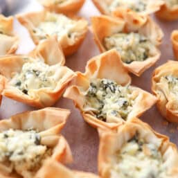 Spinach and artichoke mini phyllo cups ready to be served on a brown platter.