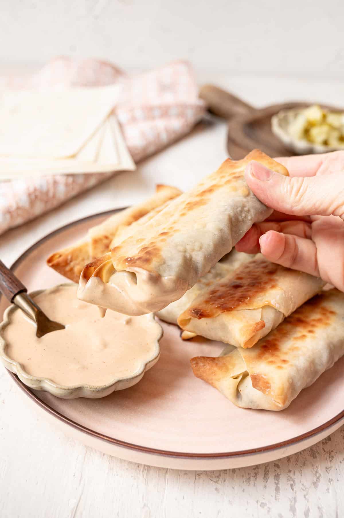 A cheeseburger egg roll being dipped into a bowl of secret sauce.