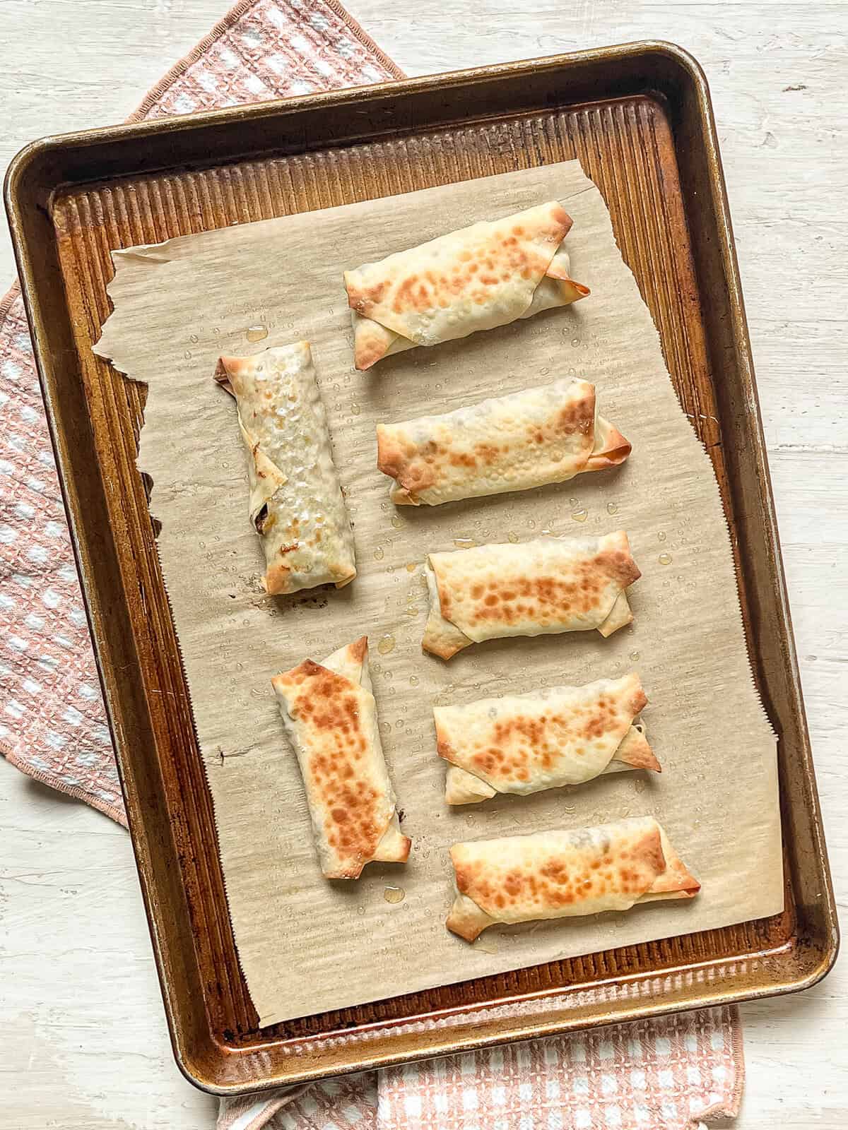 Cheeseburger egg rolls on a parchment-lined baking sheet straight from the oven.