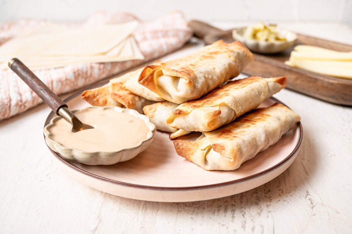 A bowl of secret sauce and a plate of cheeseburger egg rolls ready to eat.