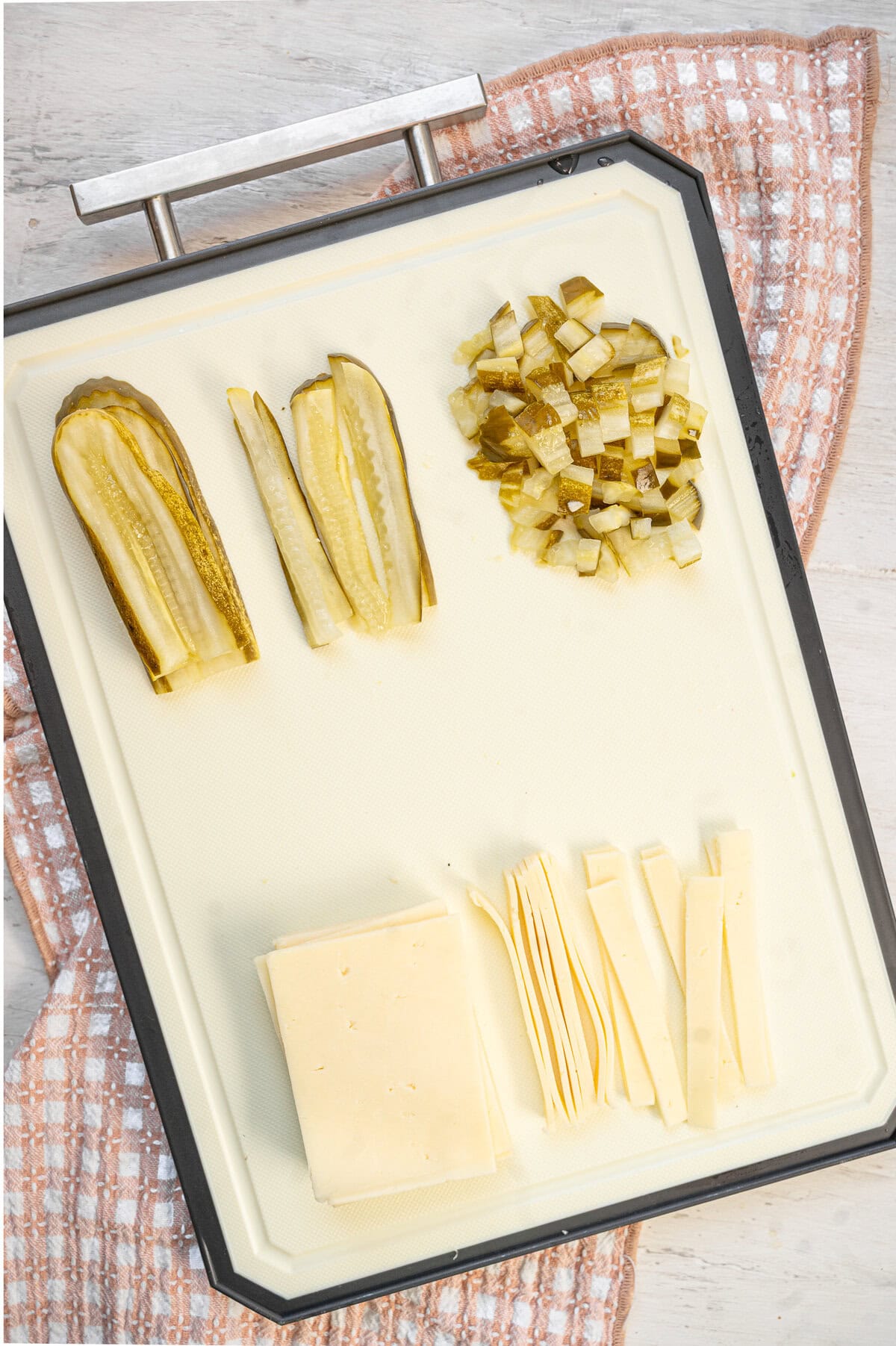 A cutting board showing strips of cheddar cheese and diced dill pickle being cut.