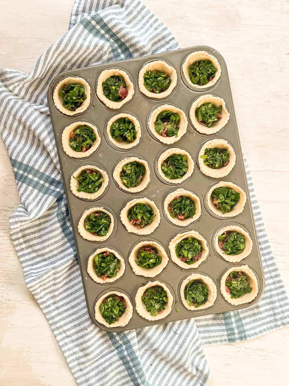 Pie crusts in a mini muffin tin with bacon and then spinach in it.