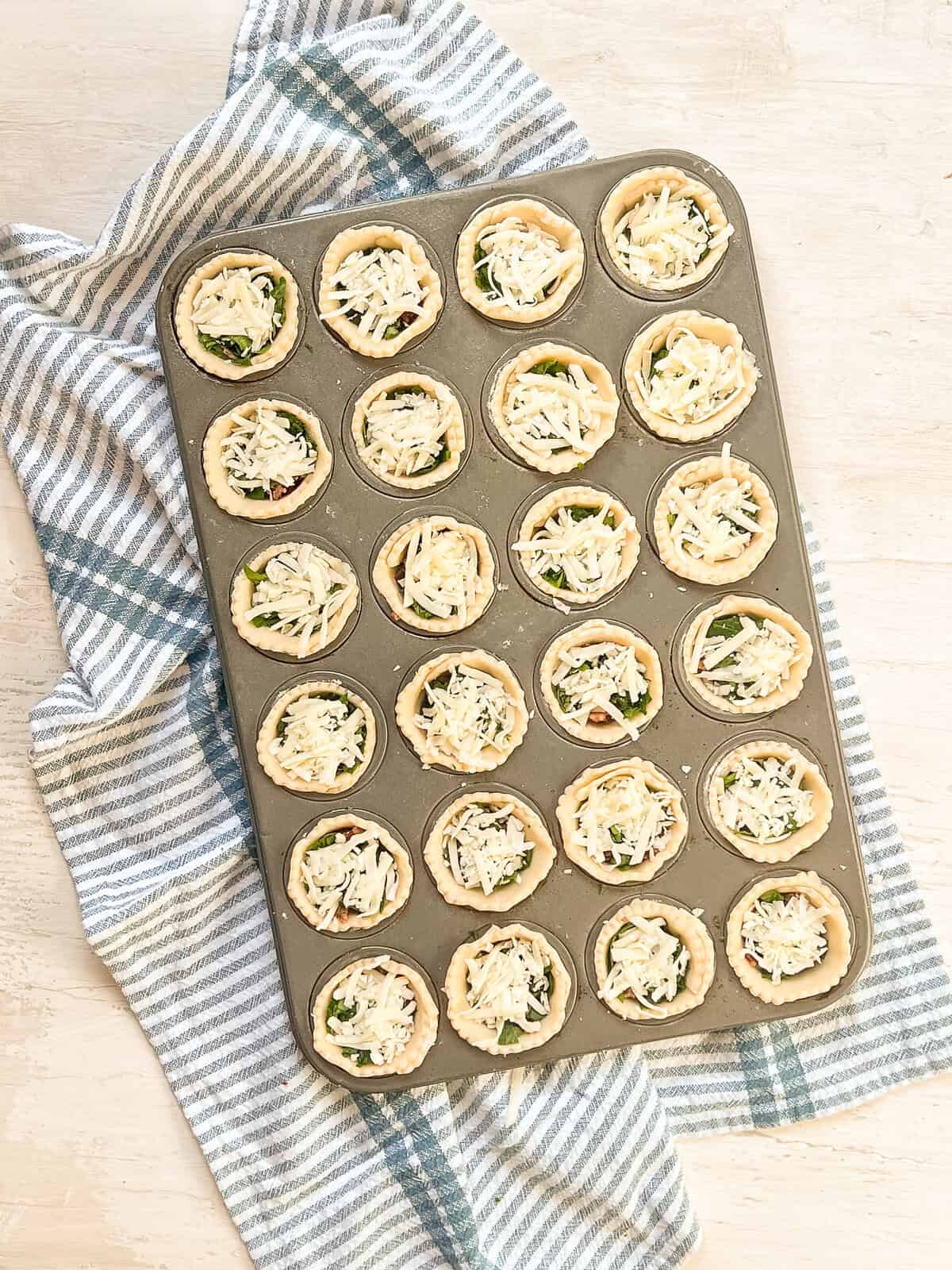 Pie crusts layered with spinach, bacon, and cheese in a mini muffin tin.