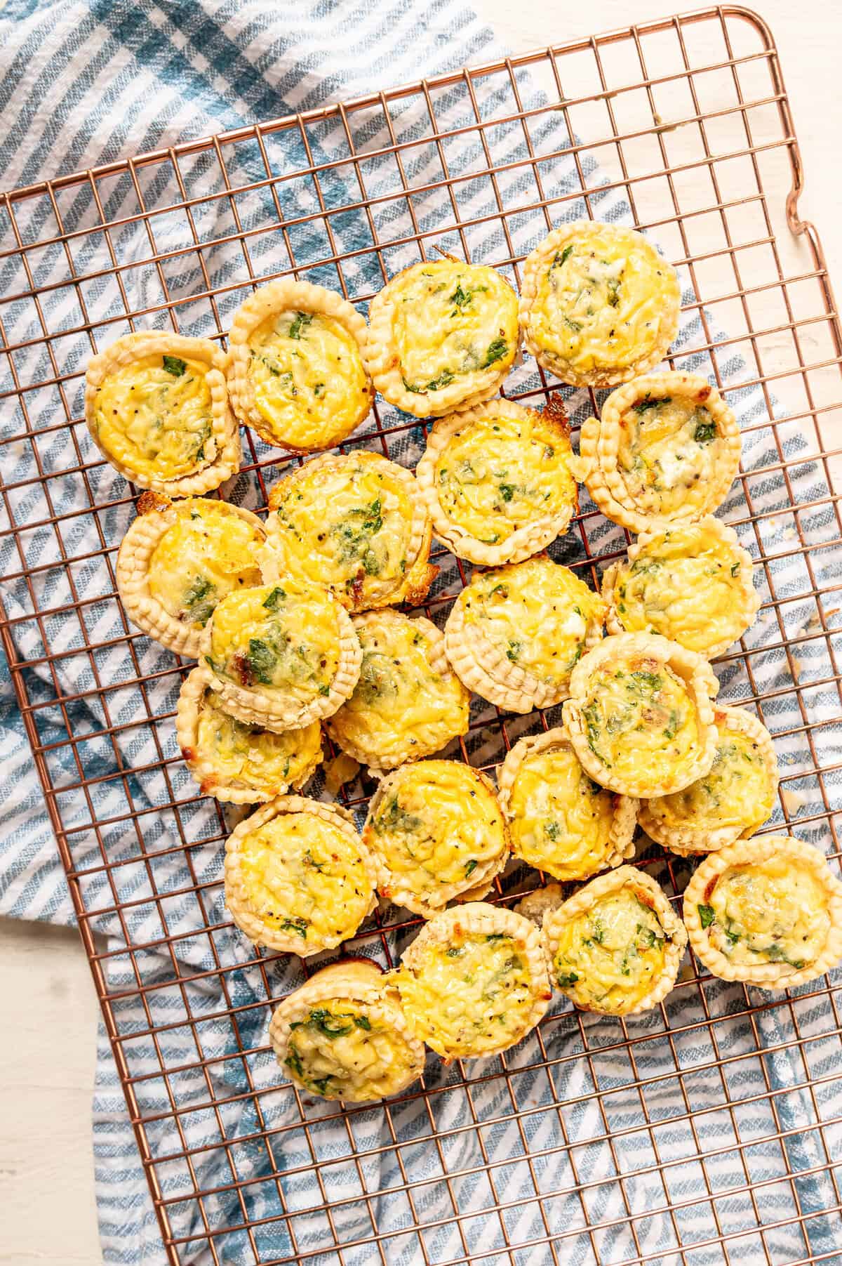 A cooling rack stacked with mini spinach and bacon quiche.
