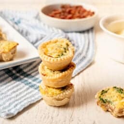 Three mini quiche stacked on top of each other with a platter of mini quiche in the background.