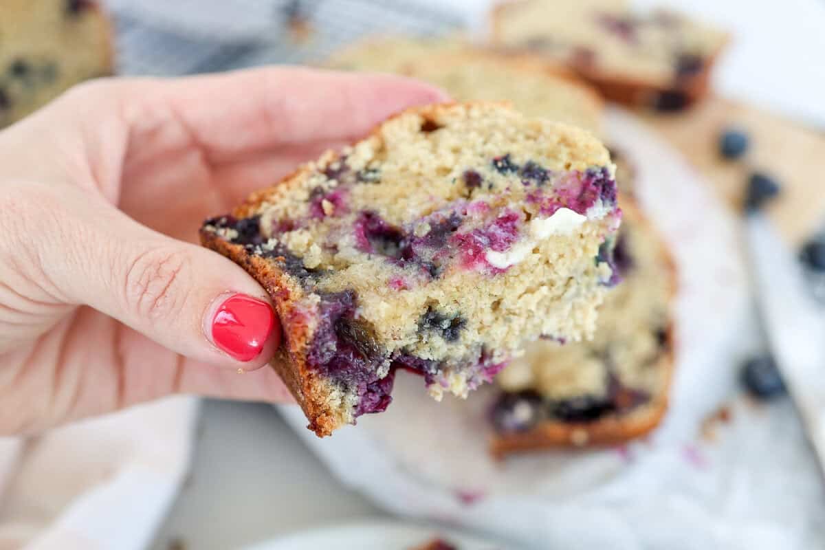 A bite out of a slice of blueberry banana bread with butter.