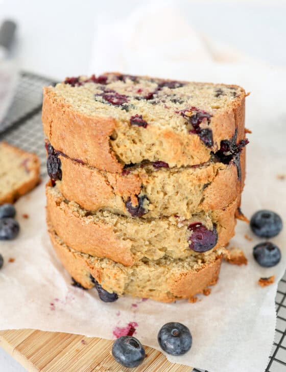 Blueberry banana bread slices stacked on a baking rack with parchment paper.
