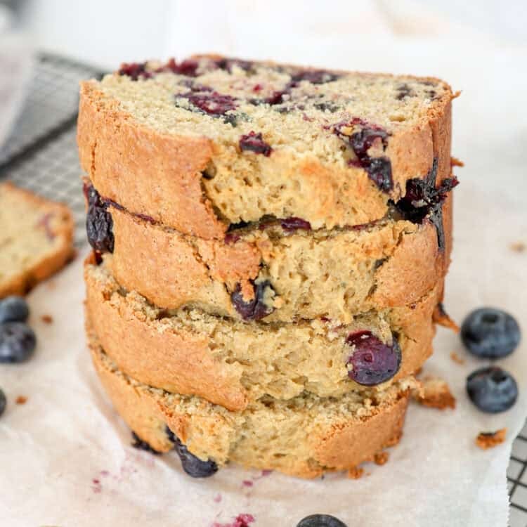 Blueberry banana bread slices stacked on a baking rack with parchment paper.
