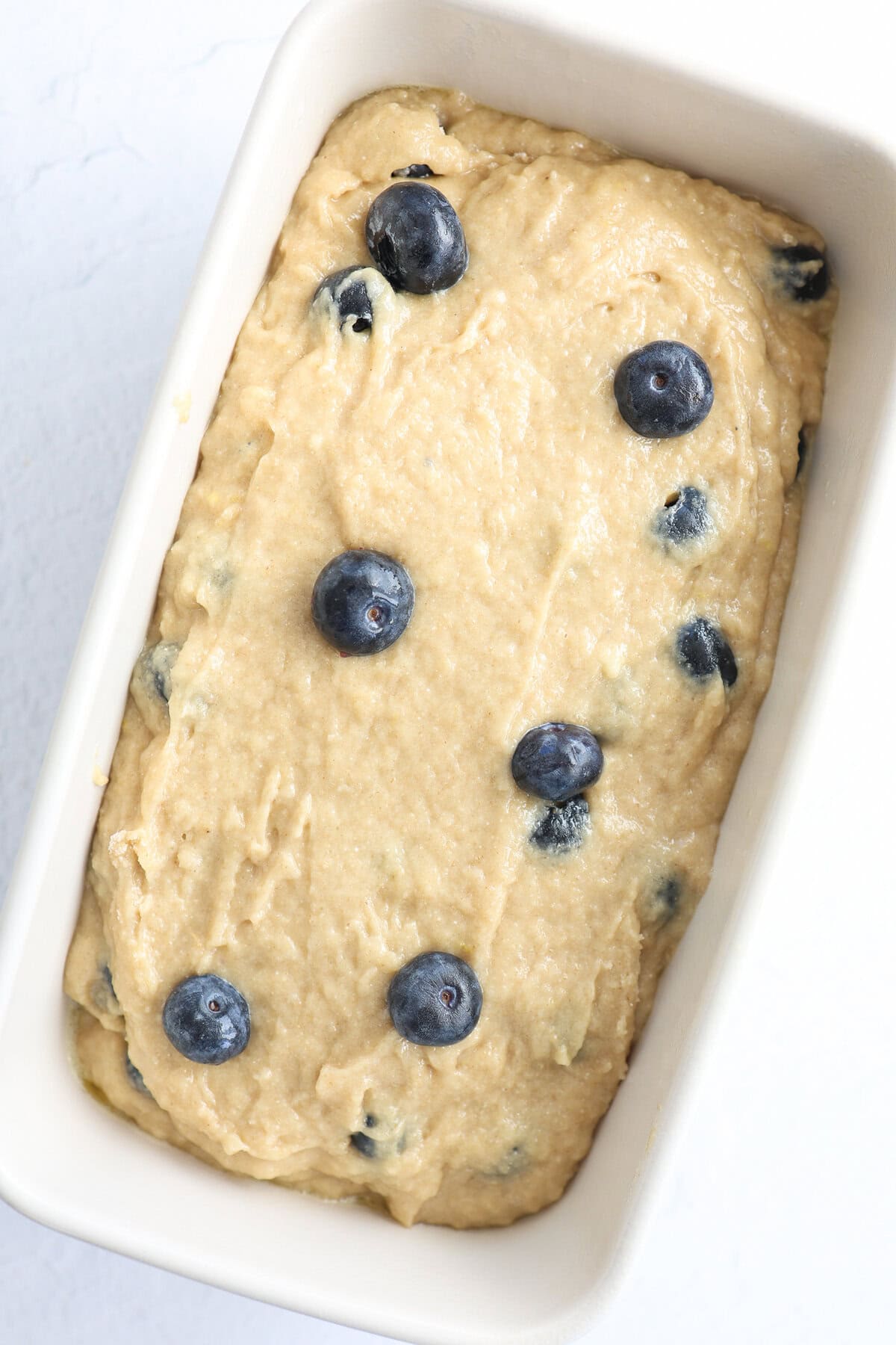 A loaf pan with blueberry banana bread batter spread in it ready to bake.