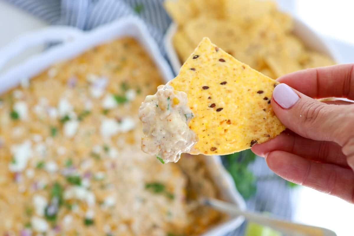 A tortilla chip being dipped into a Mexican street corn dip.