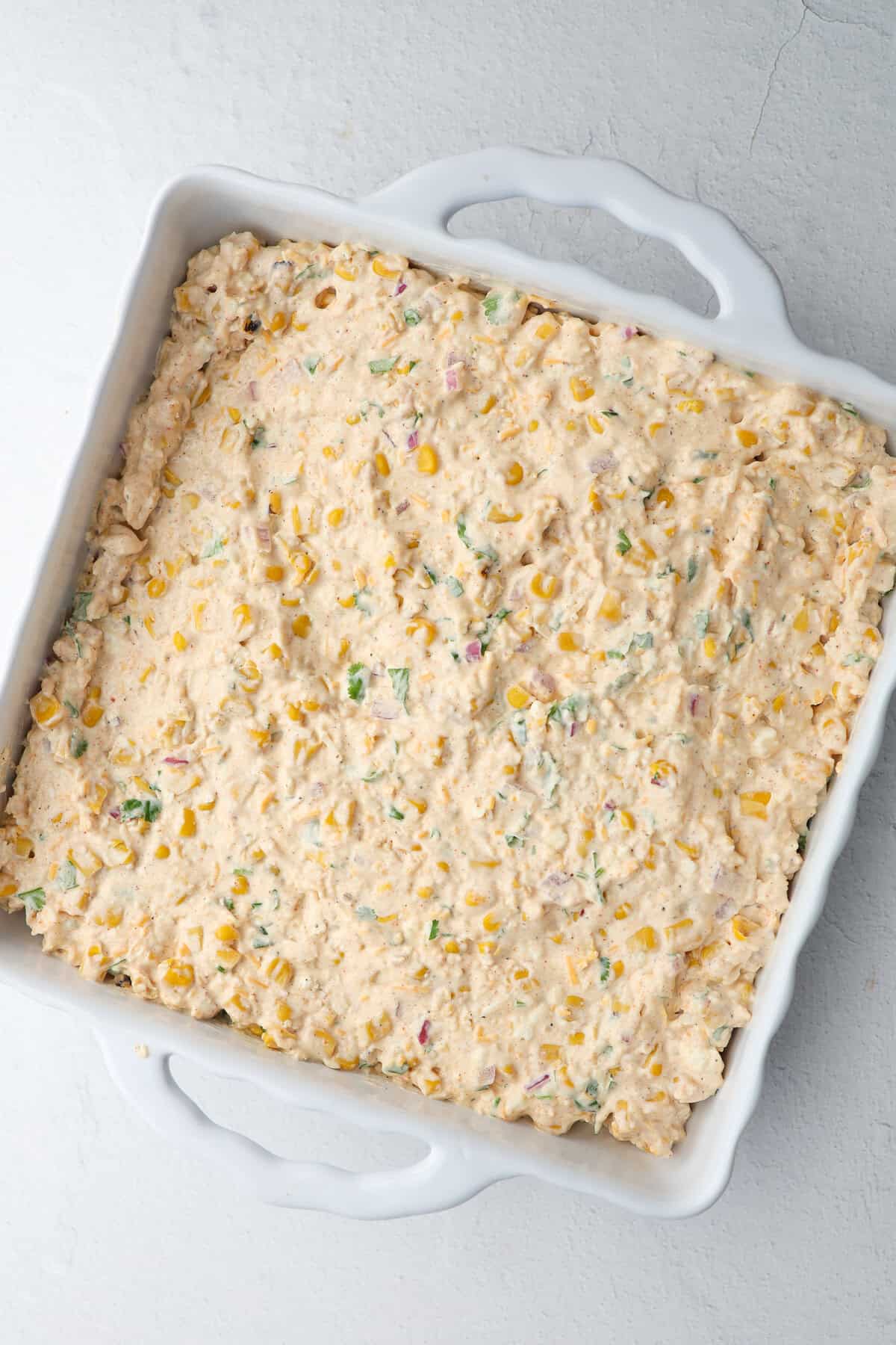 Mexican street corn dip spread in a square casserole dish ready to bake.