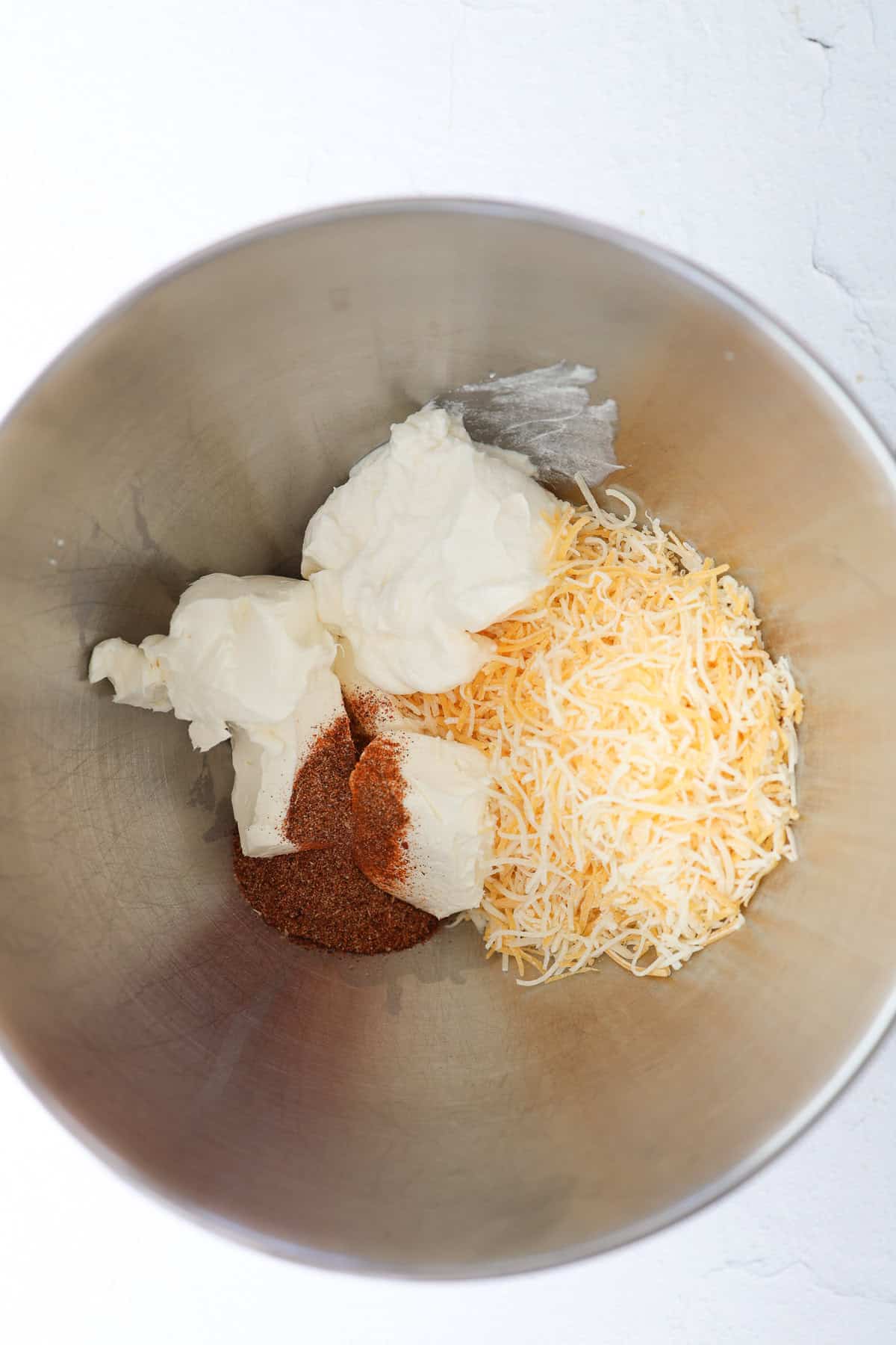 Sour cream, cream cheese, taco seasoning, and shredded Mexican cheese in a bowl before mixing.