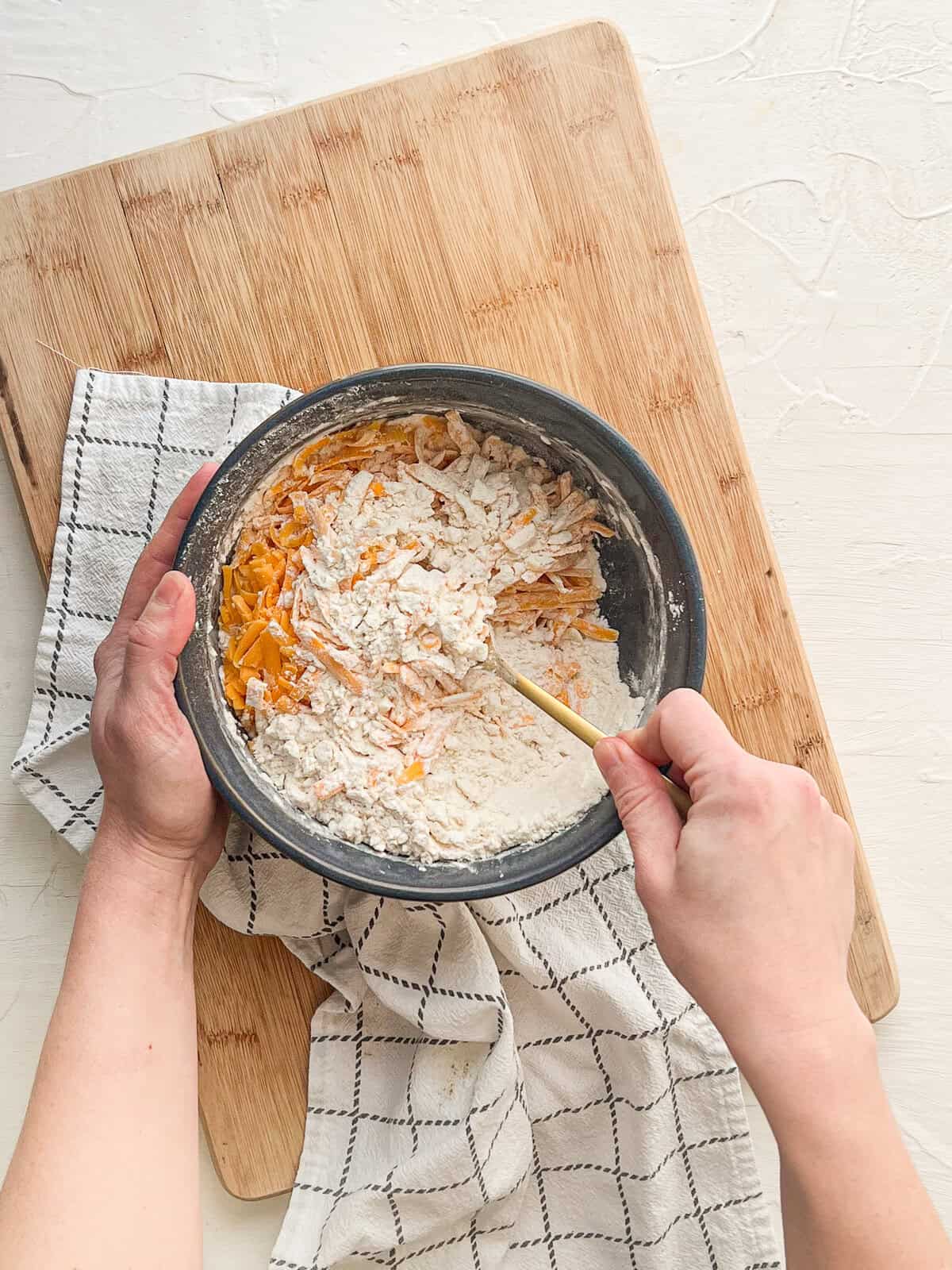 Freshly shredded cheddar being mixed into biscuit batter.