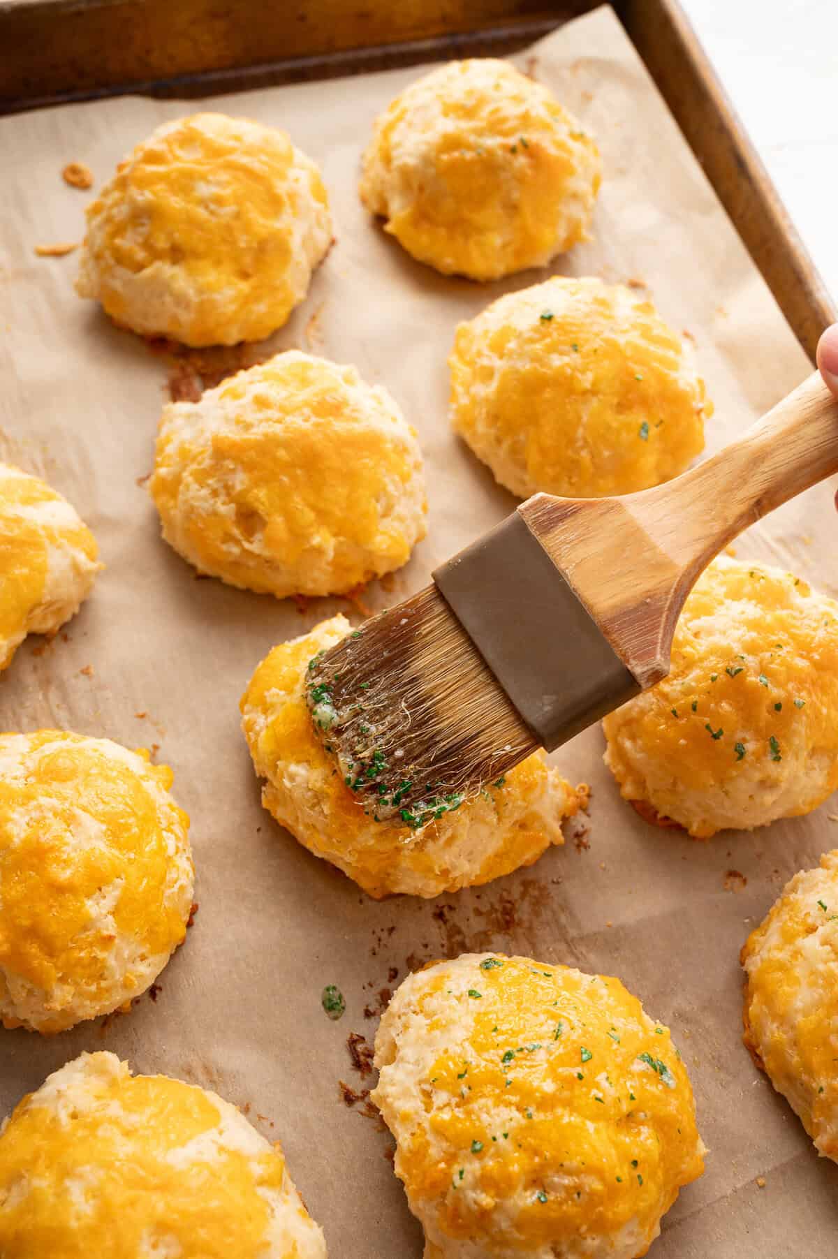 A pastry brush putting melted butter and seasonings on top of biscuits.