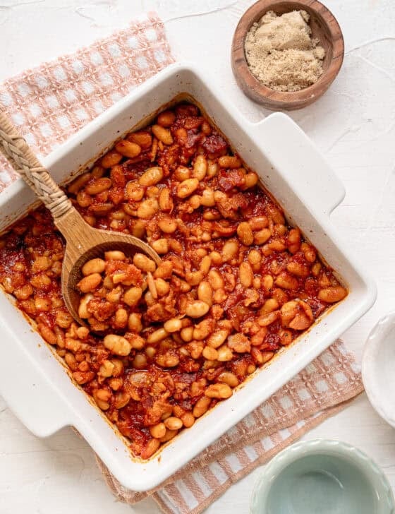 A wooden spoon serving baked beans from a white casserole dish.