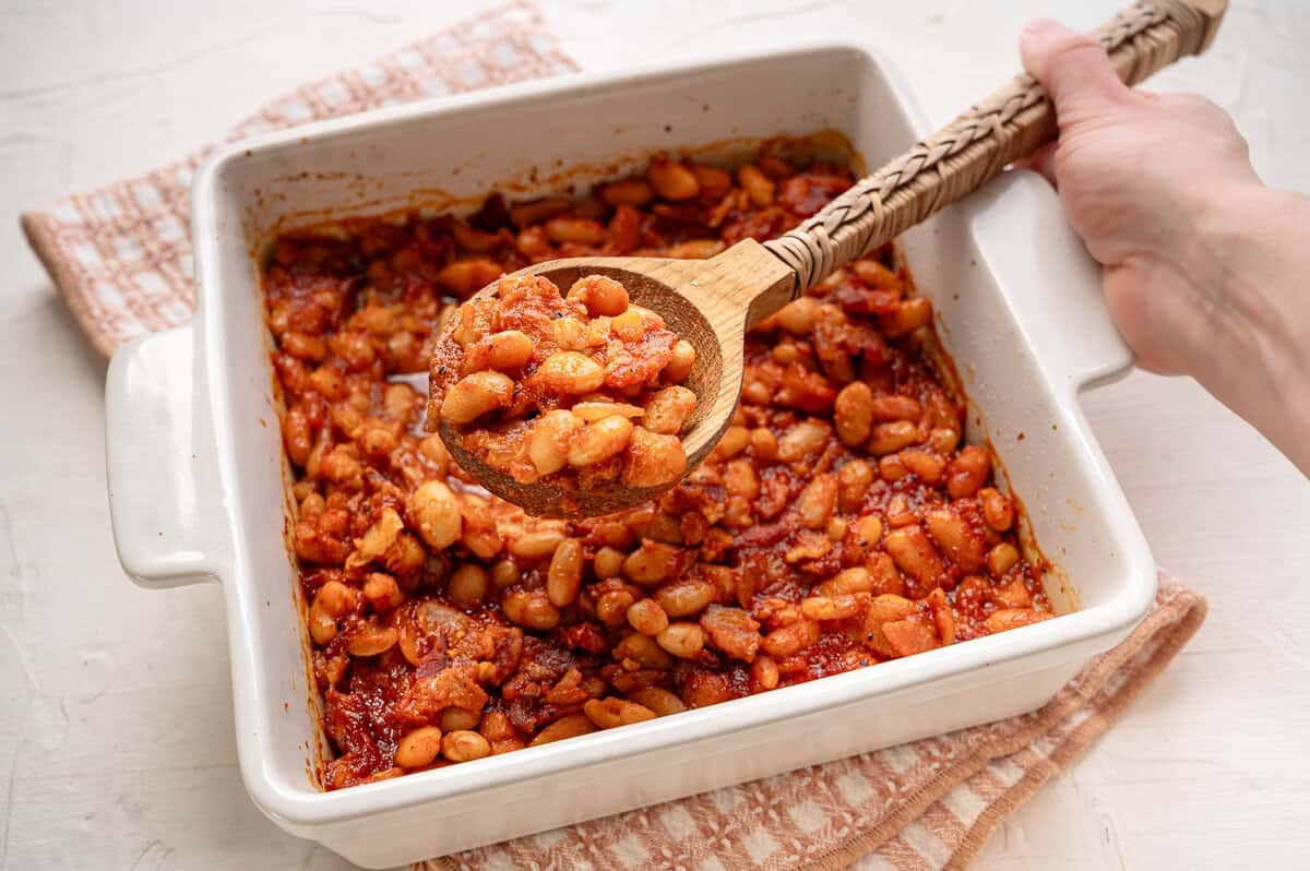 A spoonful of baked beans being held above the casserole dish of beans.