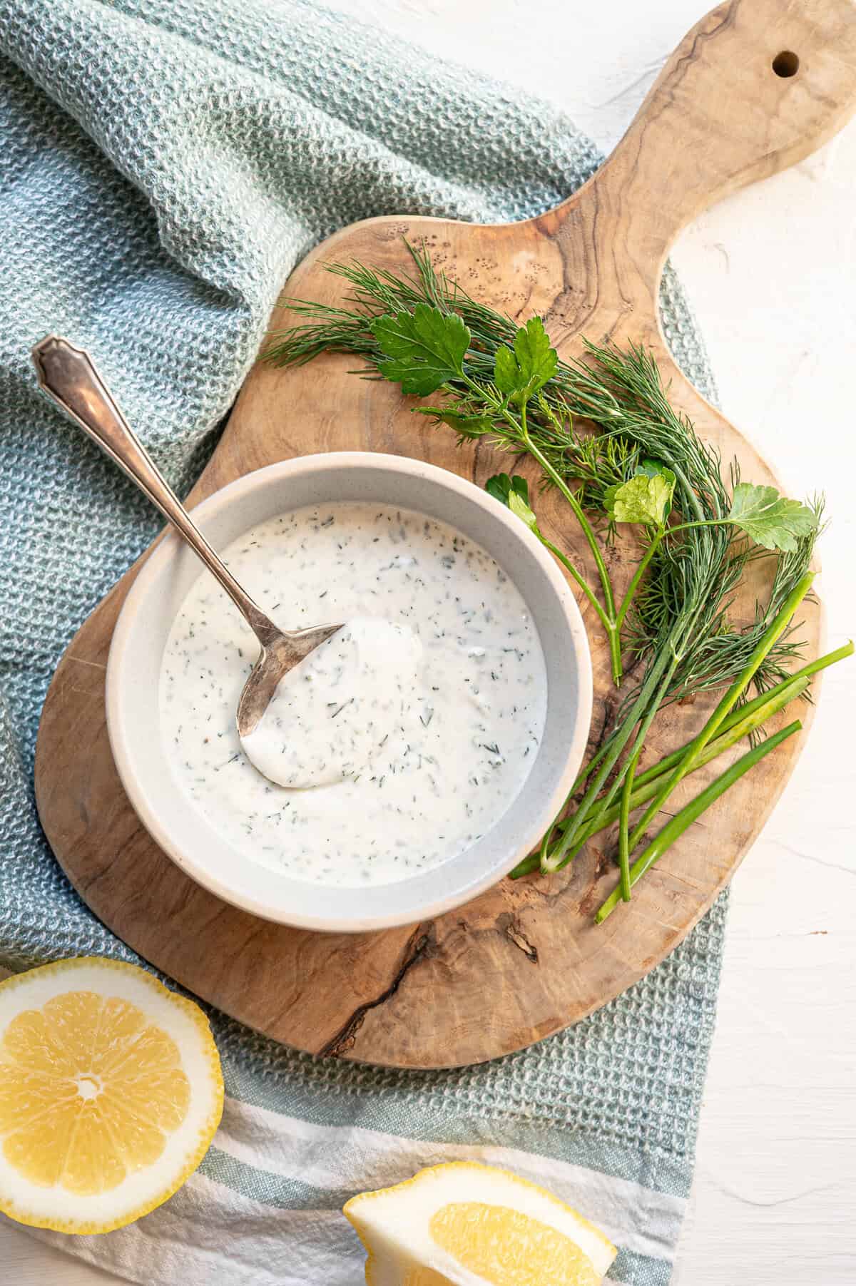 A bowl of homemade ranch dressing on a wooden cutting board with a spoon.
