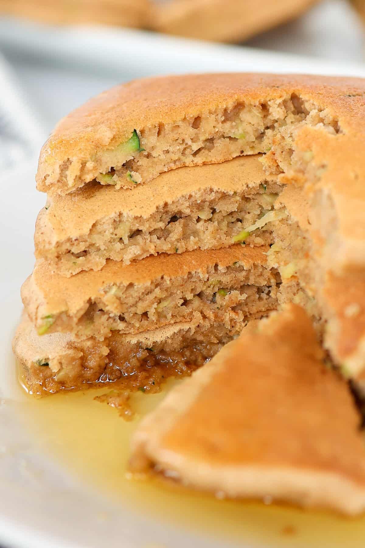 Four zucchini pancakes stacked in a pool of maple syrup.