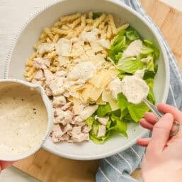Homemade Caesar dressing being spooned on a bowl with pasta, cooked chicken, chopped Romaine lettuce, and shaved Parmesan.