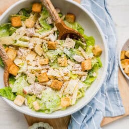 Caesar pasta salad served with two wooden salad tongs and a small dish of ground pepper next to it.