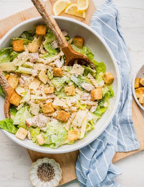 Caesar pasta salad served with two wooden salad tongs and a small dish of ground pepper next to it.