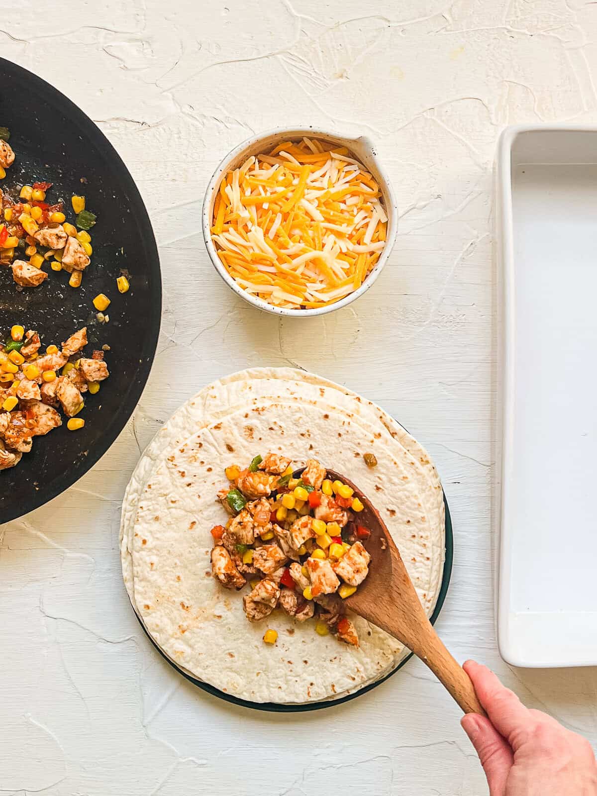A spoon scooping the filling for chicken fajita casserole into a tortilla.