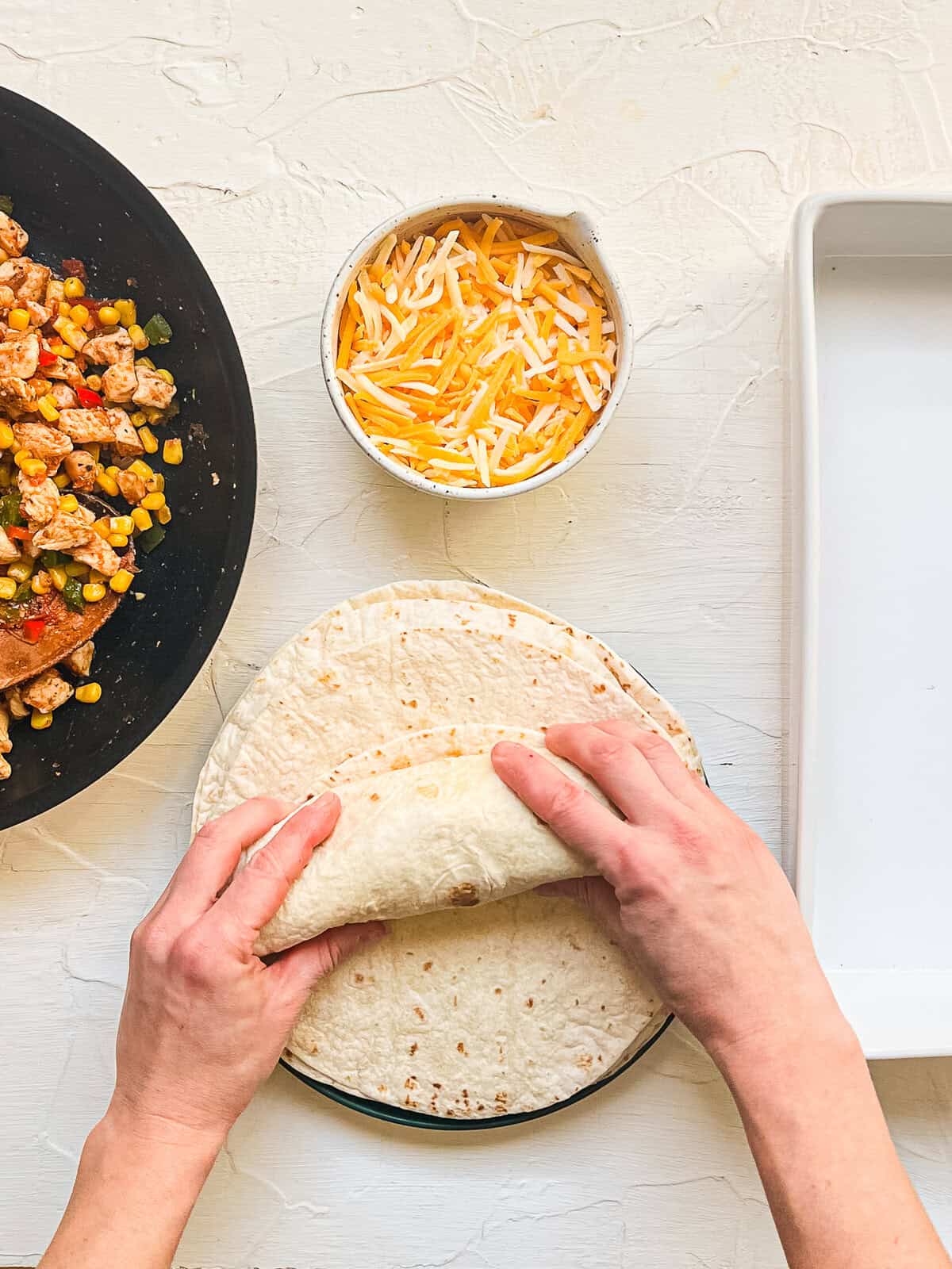 Hands wrapping up a tortilla that is filled with chicken and veggie filling.