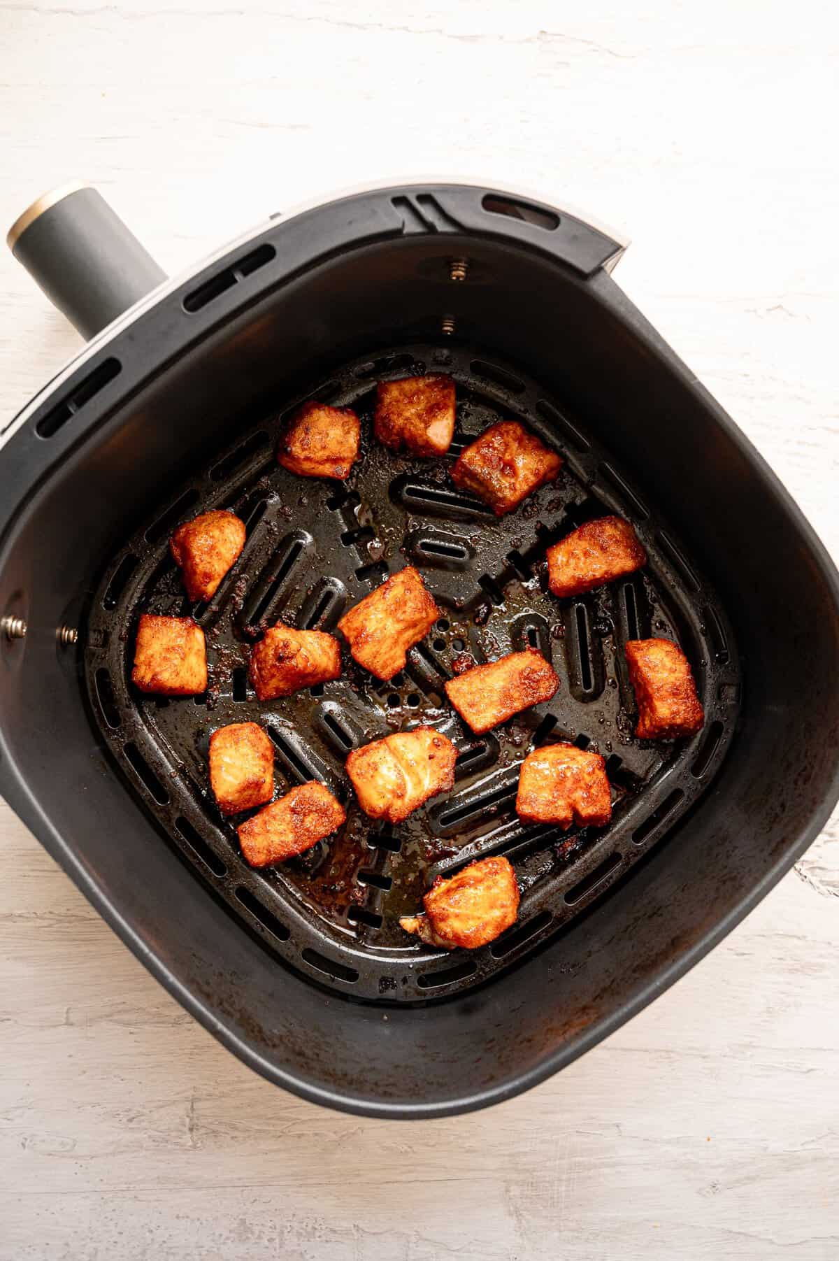 Salmon bites in an air fryer basket after being cooked.