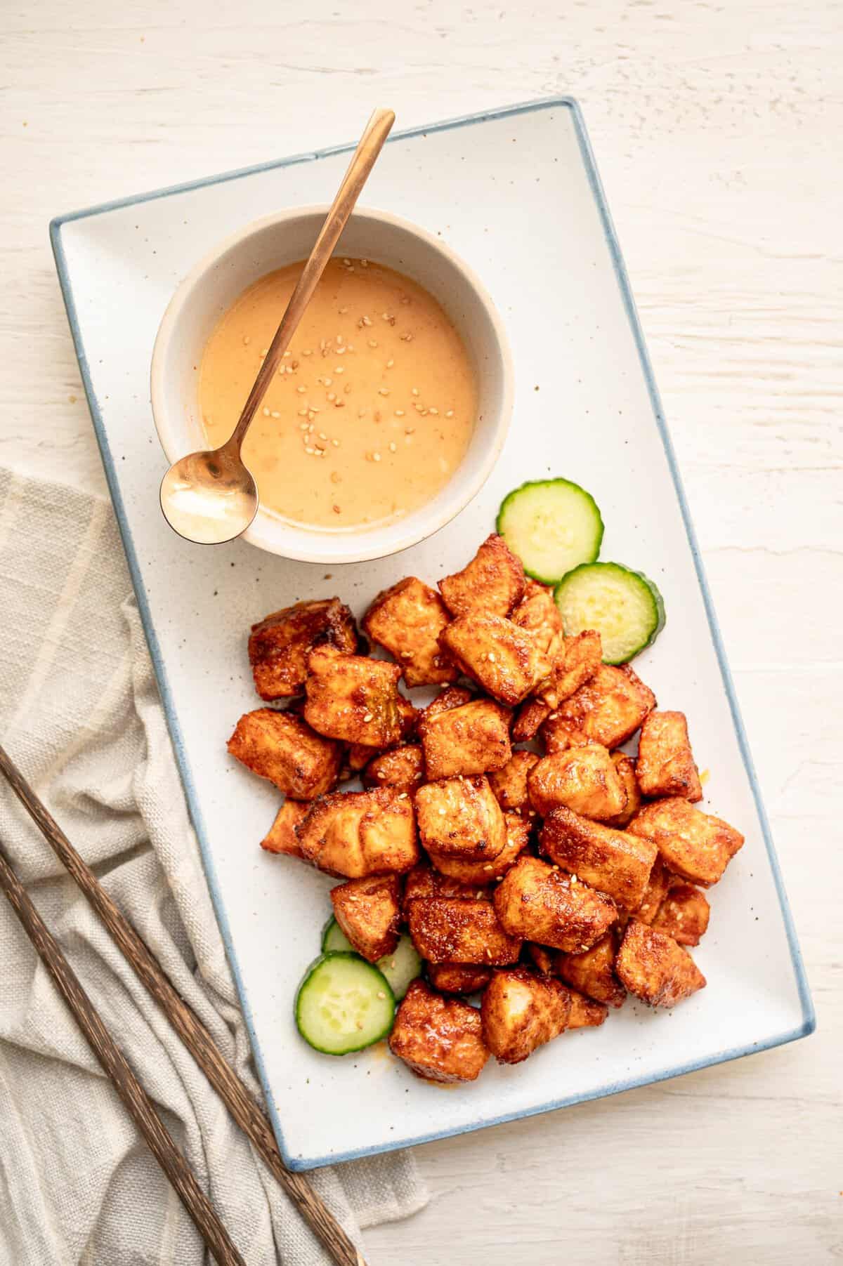 Salmon bites on a platter with a bowl of bang bang sauce on it.