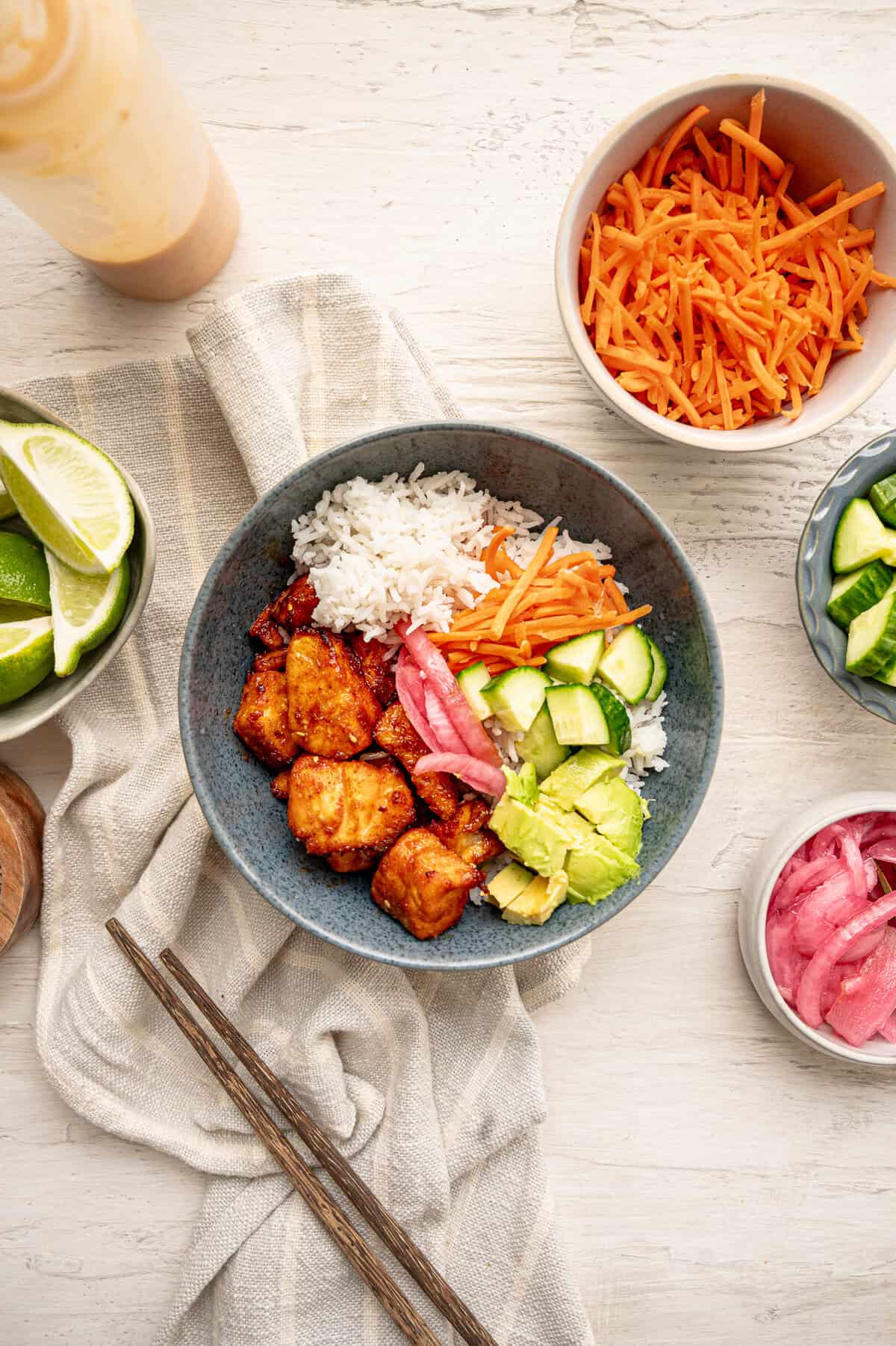 A bang bang salmon bowl with rice, avocado, rice, cucumber, shredded carrots and pickled red onions.