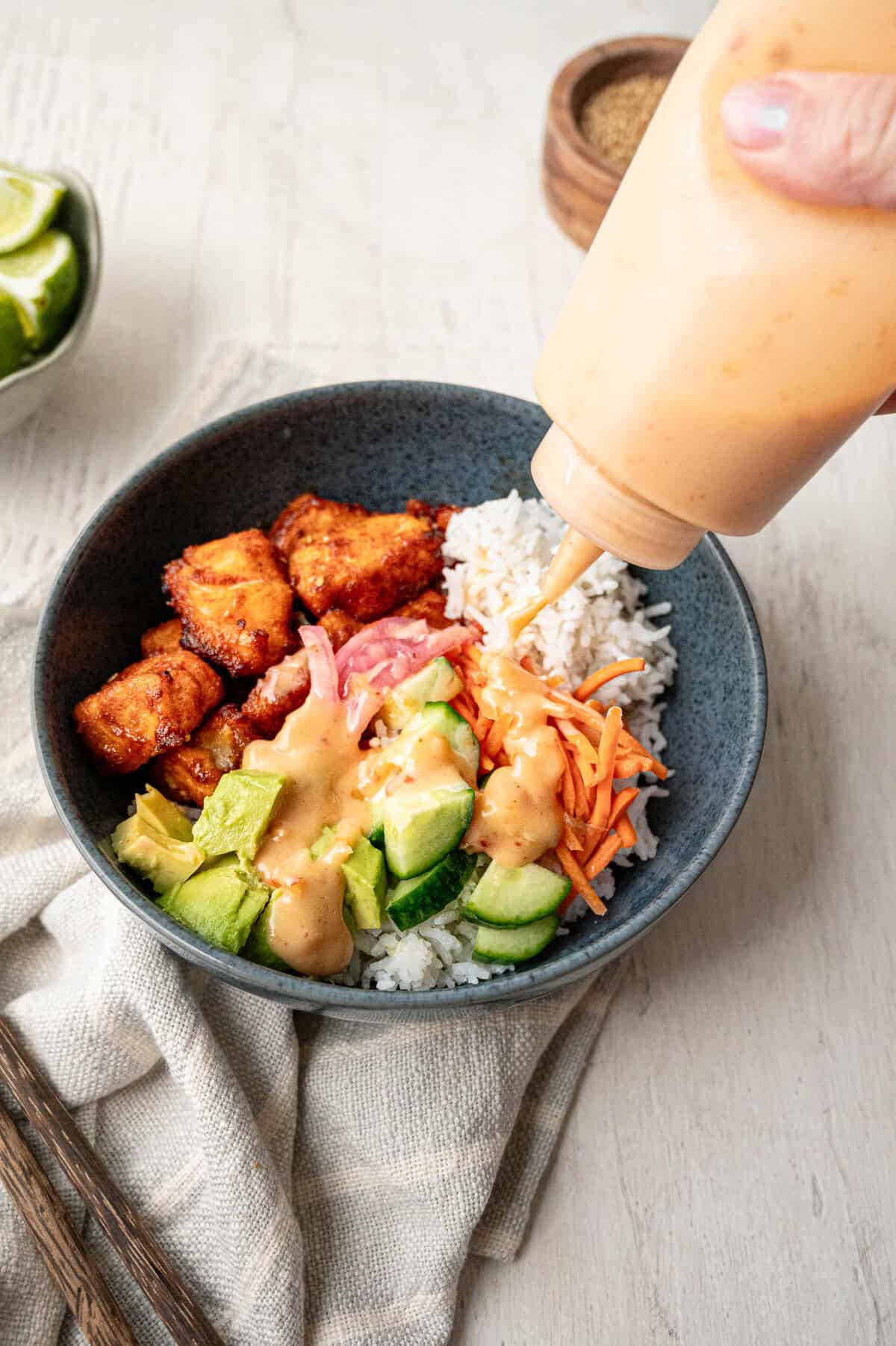 Bang Bang Sauce being squeezed on to a bowl with rice, salmon bites, pickled red onion, avocado, carrots and cucumbers.