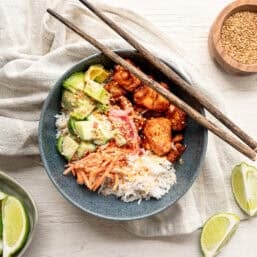 Chopsticks resting on a bowl with rice, salmon bites, and other toppings including bang bang sauce.