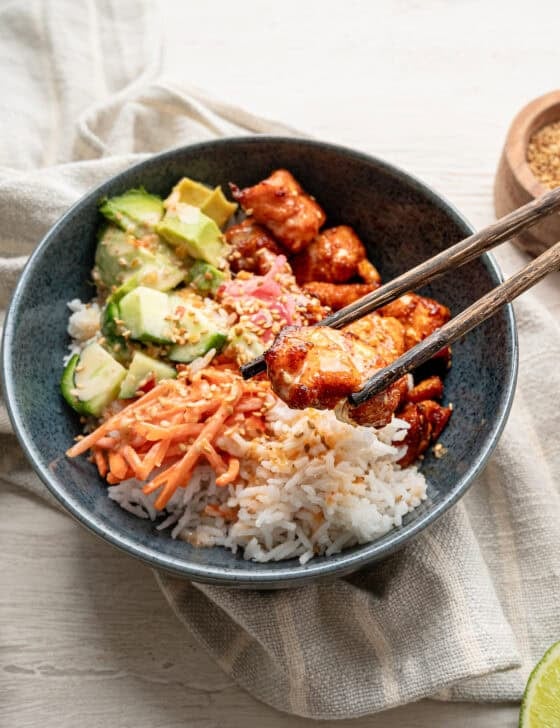 Chopsticks lifting a bite of salmon out of a bang bang salmon bowl.
