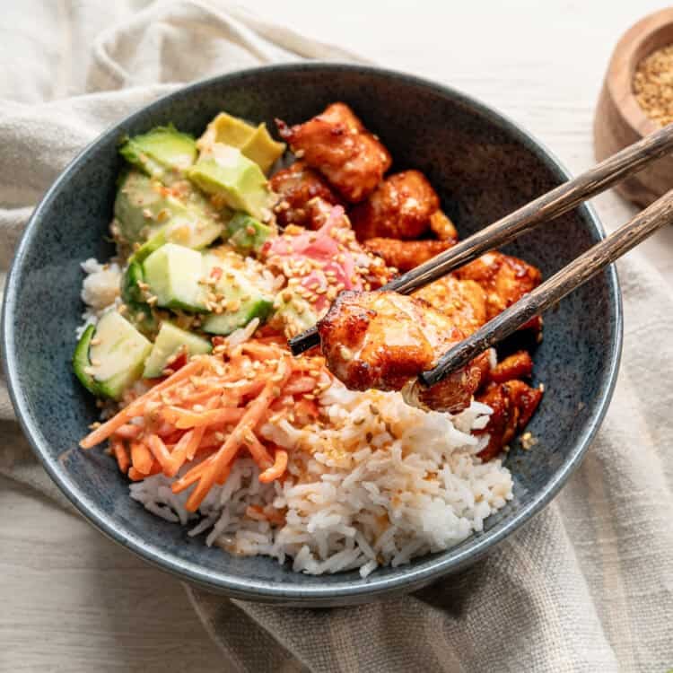 Chopsticks lifting a bite of salmon out of a bang bang salmon bowl.