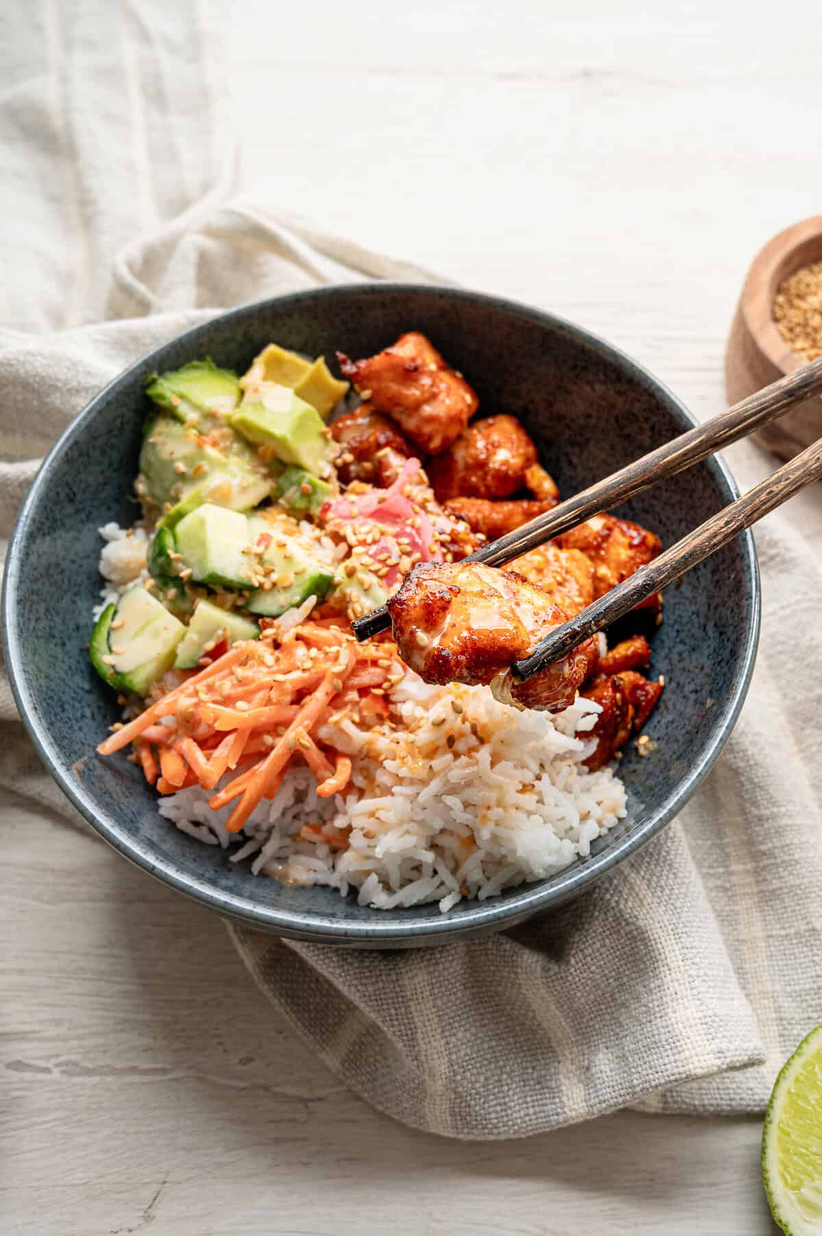 Chopsticks lifting a bite of salmon out of a bang bang salmon bowl.