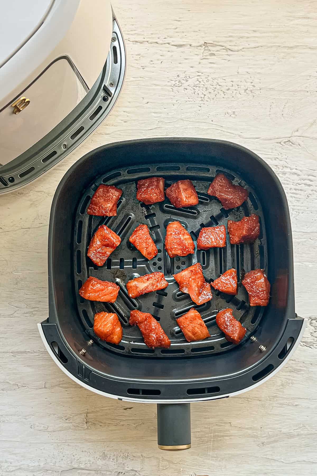 Bite-sized raw salmon with seasonings in an air fryer basket ready to be cooked.