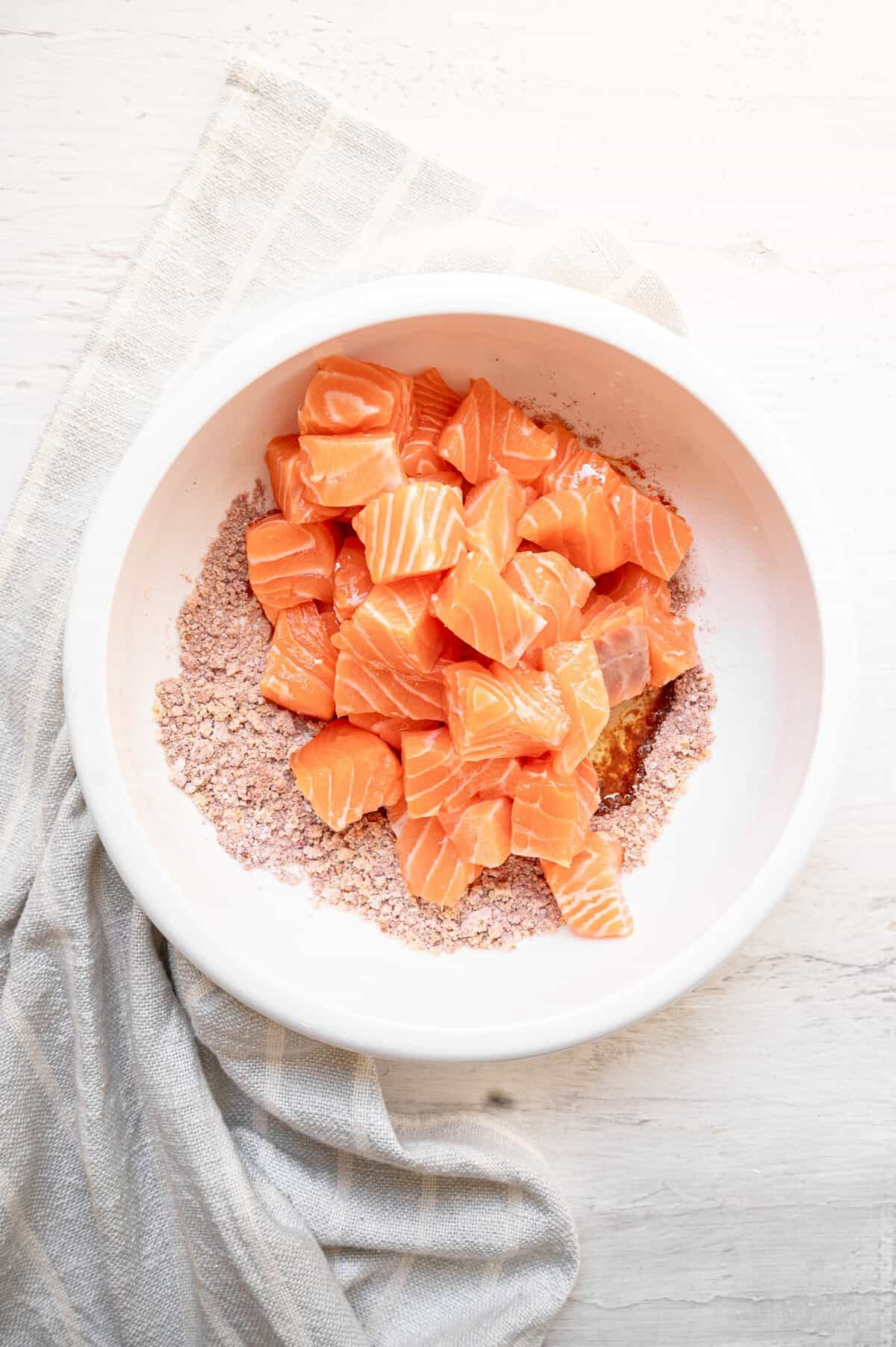 Bite-size pieces of salmon filets being tossed in seasonings.
