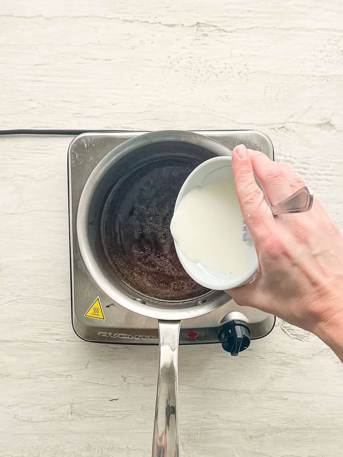 Corn starch slurry being poured into a sauce pan with teriyaki sauce ingredients.